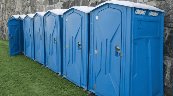 Row of blue portable toilets lined up on grass against a stone wall for event sanitation in Worcester, MA
