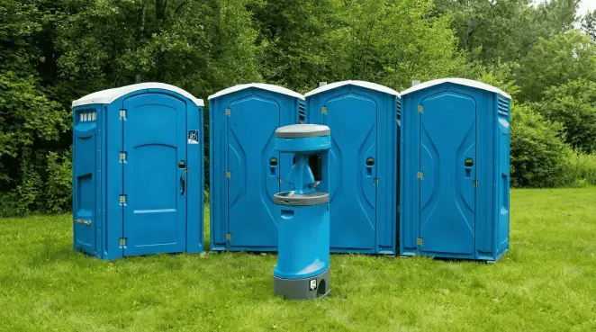 Four blue portable toilets and a matching hand washing station on grass near trees, a common sight at local outdoor events in Worcester, MA