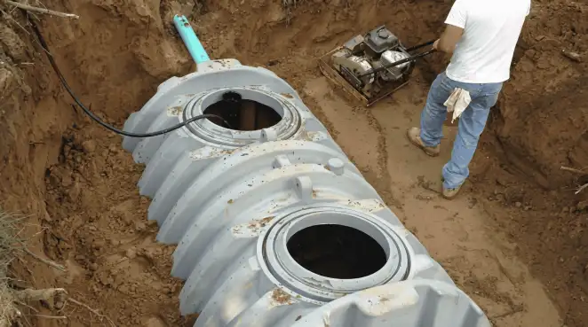 Septic tank installation showing a technician compacting soil around a new poly septic tank in an excavation pit in Worcester, MA
